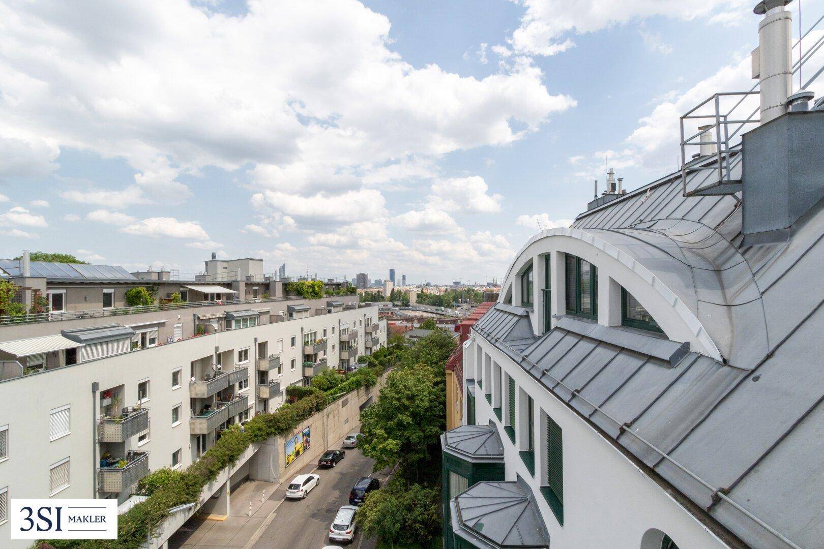 Panoramablick über die Stadt mit verschiedenen Dächern und Gebäuden unter blauem Himmel.