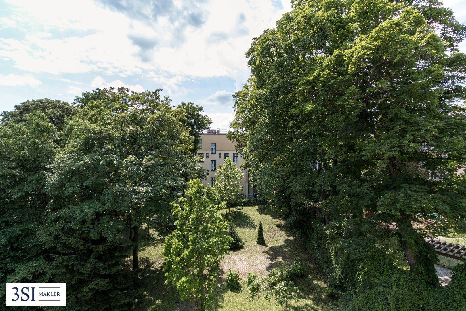 Grüner Garten mit hohen Bäumen und einem Gebäude im Hintergrund unter bewölktem Himmel.