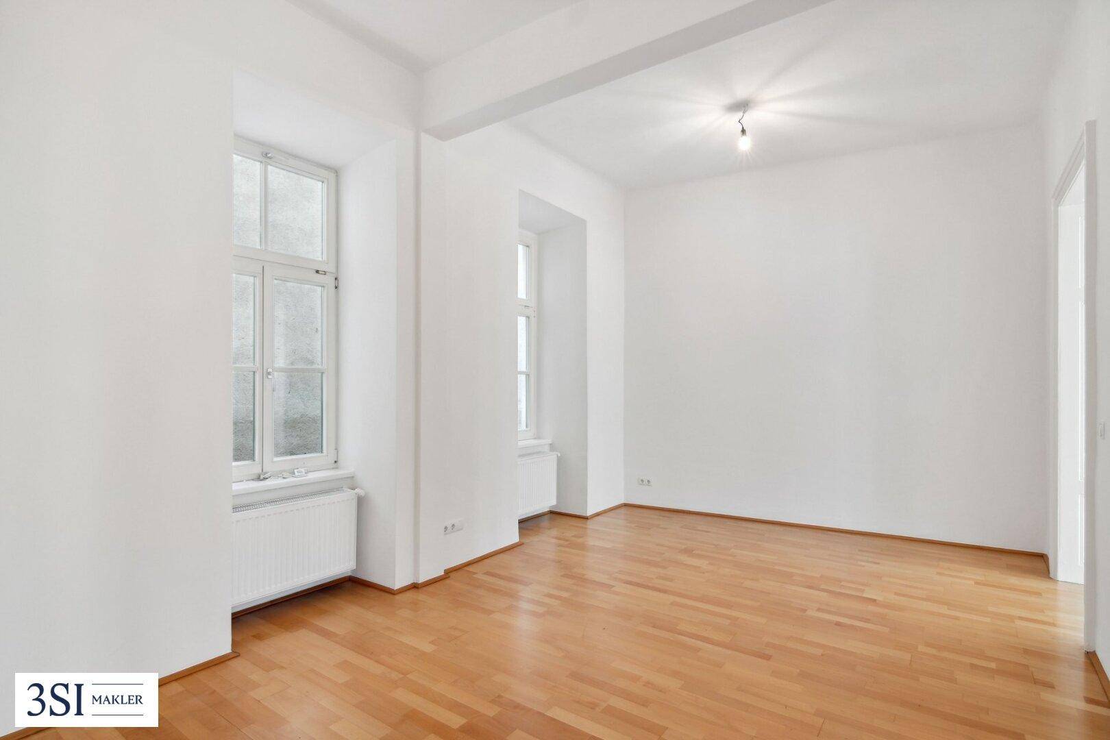 Helles, leeres Zimmer mit Parkettboden und hohen Fenstern, bereit zur individuellen Gestaltung.