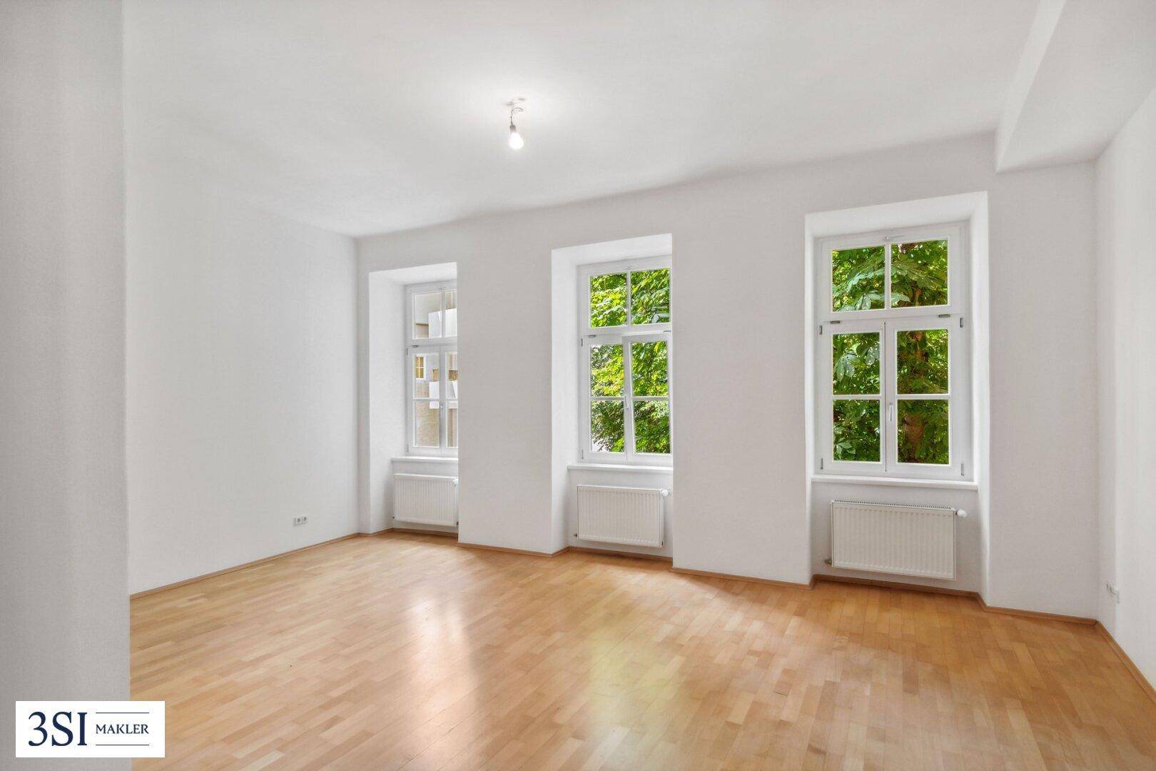 Heller Raum mit Parkettboden und Blick ins Grüne durch die großen Fenster.