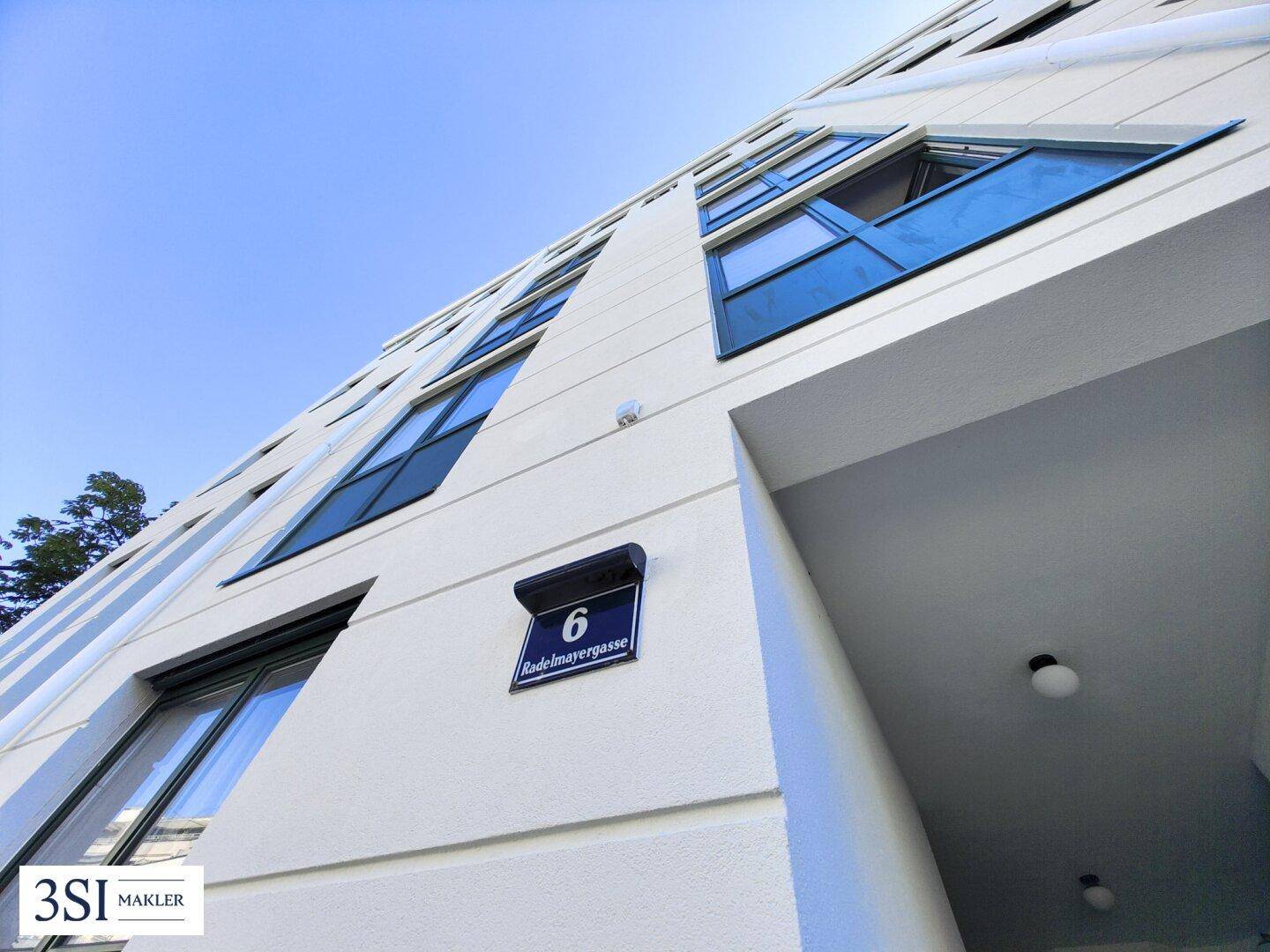 Detailansicht der modernen Fassade mit Hausnummer 6 und blauen Fenstern unter klarem Himmel.