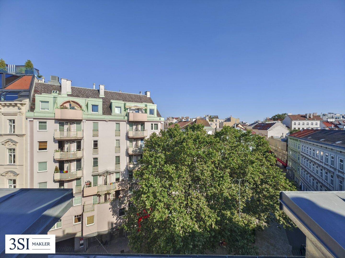 Blick auf eine belebte Straße mit Bäumen und historischen Gebäuden unter blauem Himmel.