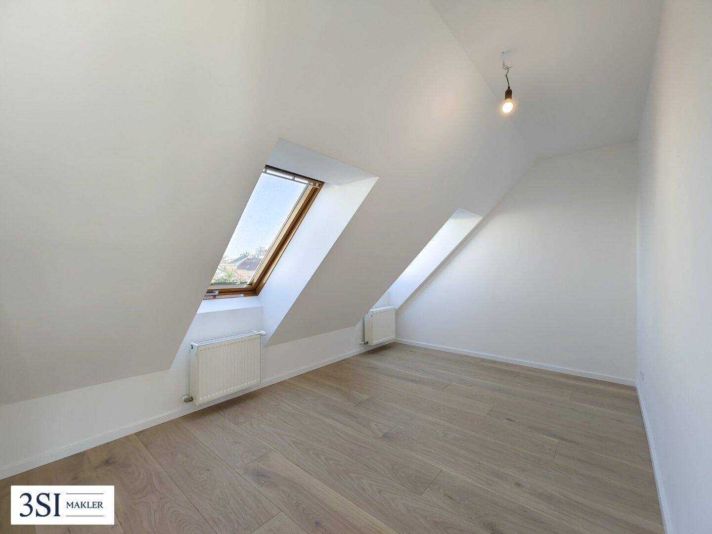 Heller Raum im Dachgeschoss mit schrägen Wänden, Dachfenstern und neuem Holzfußboden.