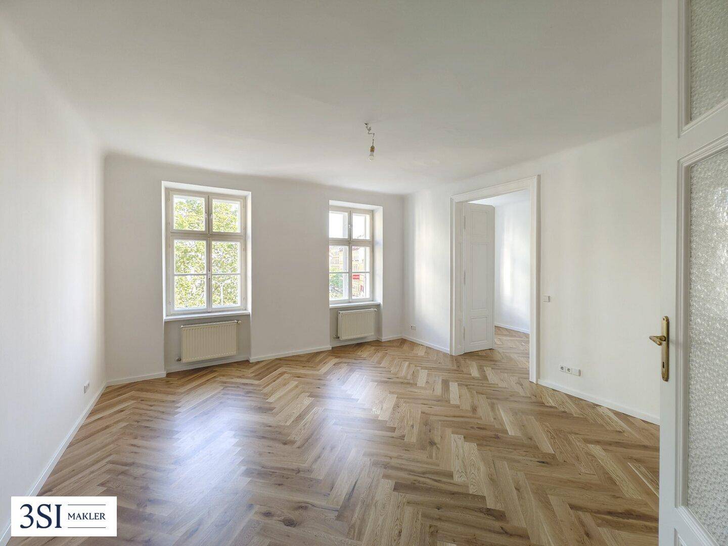 Großes Zimmer mit Fischgrätparkett und einer Doppeltür, die in einen weiteren Raum führt.