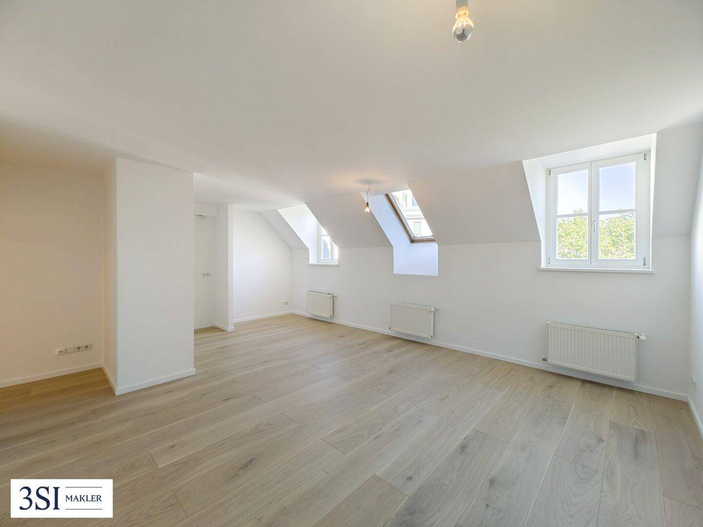 Geräumiges Dachzimmer mit Holzboden, Dachschrägen und mehreren Fenstern für viel Tageslicht.