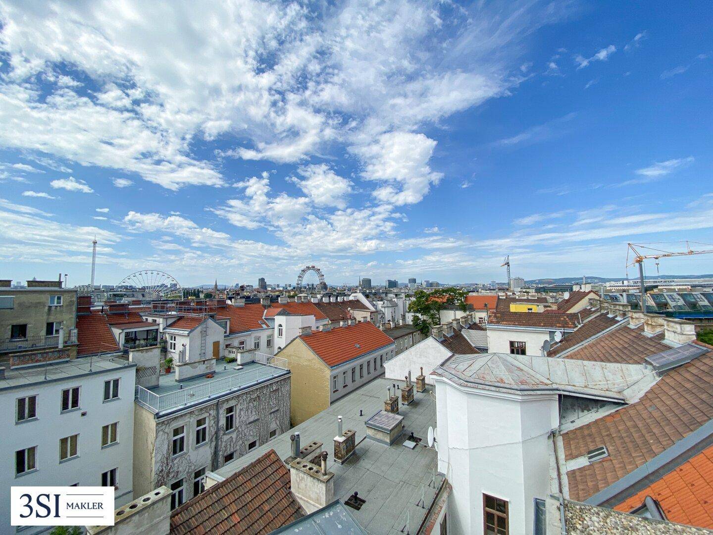 Panoramablick über die Stadt mit roten Dächern und dem Riesenrad am Horizont.