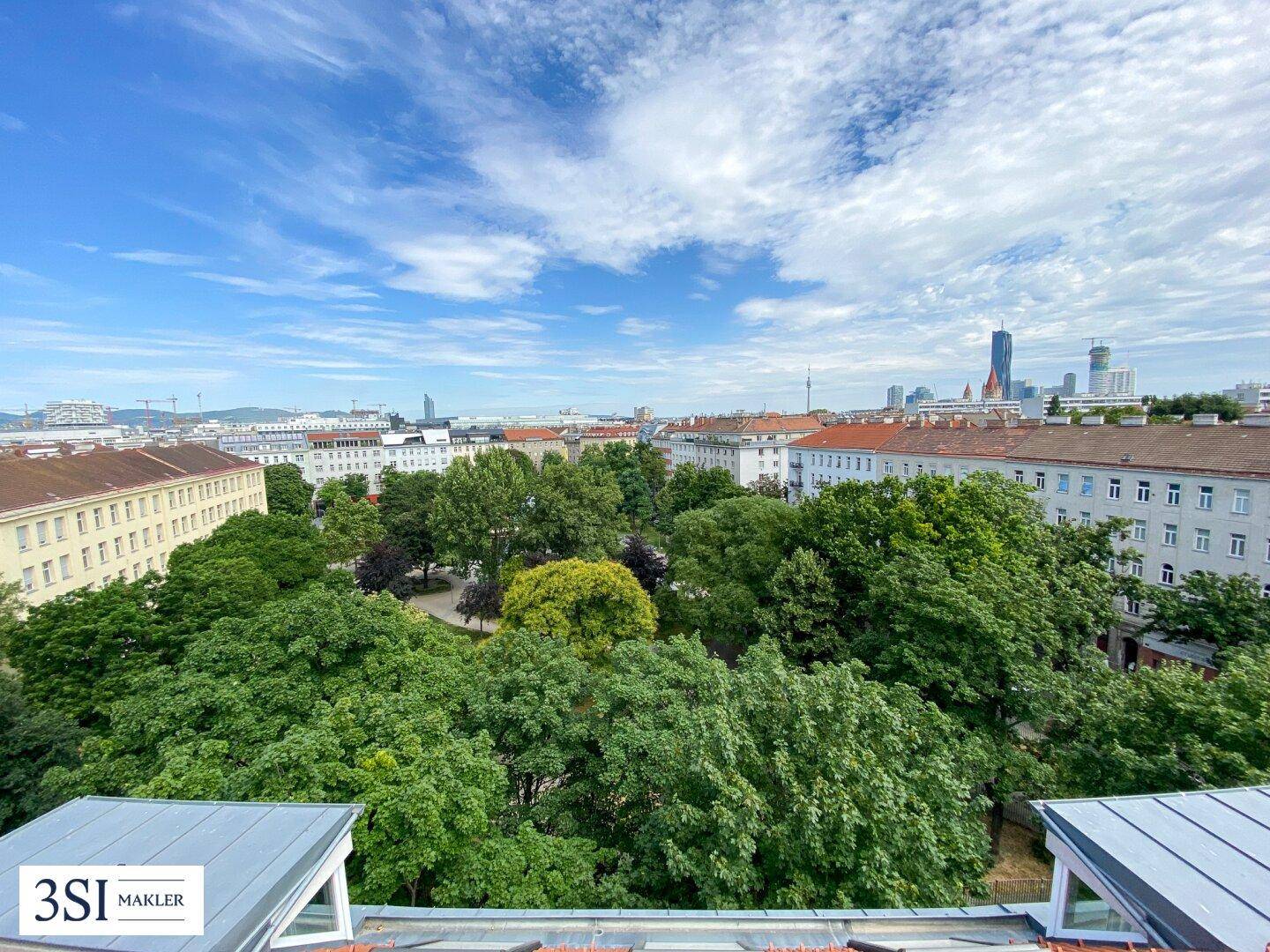 Panoramablick über einen üppigen Stadtpark mit umliegenden Gebäuden und blauem Himmel.