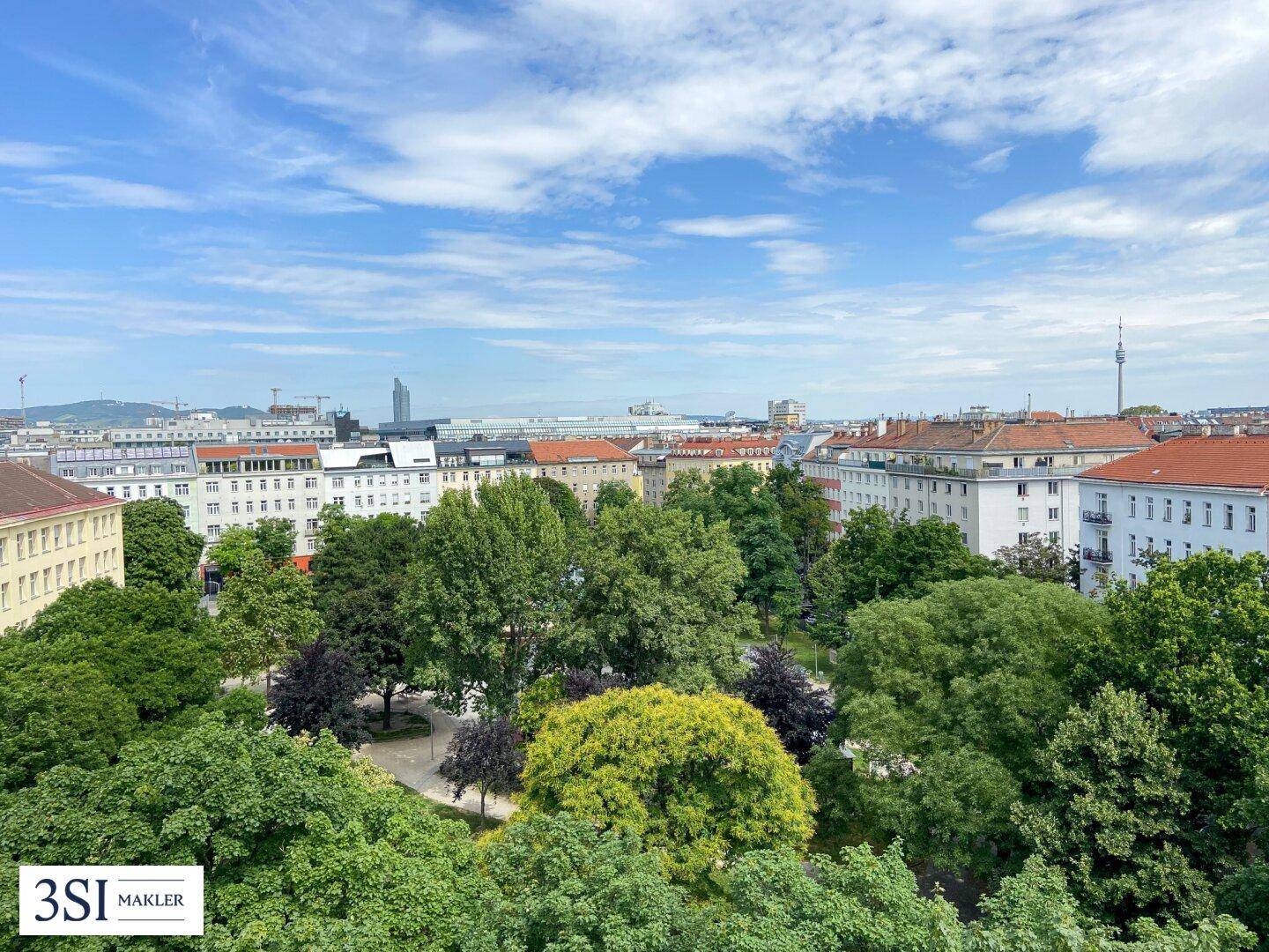 Weitläufiger Blick auf eine grüne Parkanlage und die Skyline der Stadt unter blauem Himmel.