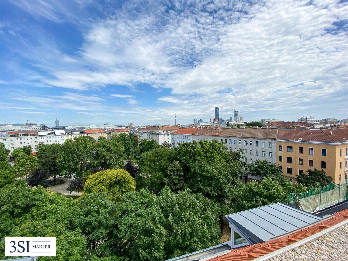 Ausblick auf einen grünen Park und die Stadtlandschaft mit modernen Gebäuden am Horizont.