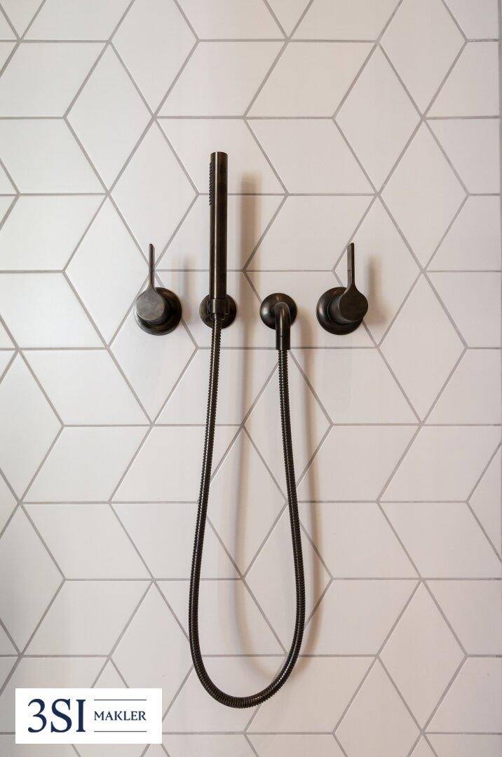 Moderne Duscharmatur mit schwarzem Finish und geometrischen Wandfliesen.