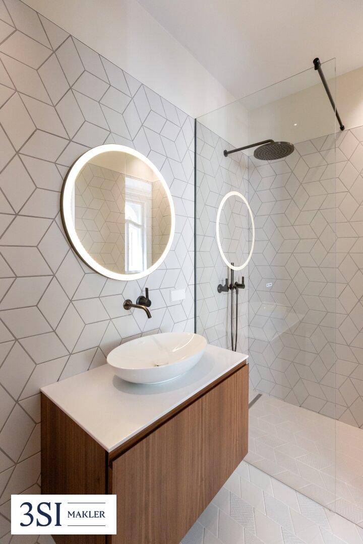 Modernes Badezimmer mit Einzelwaschbecken, beleuchtetem Spiegel und begehbarer Dusche.