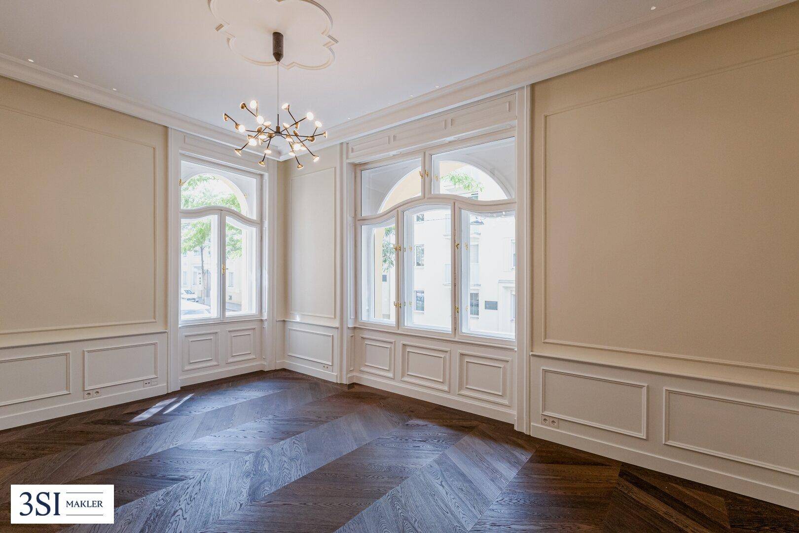 Elegantes Wohnzimmer mit Fischgrätparkett, Stuckelementen und großen Bogenfenstern.