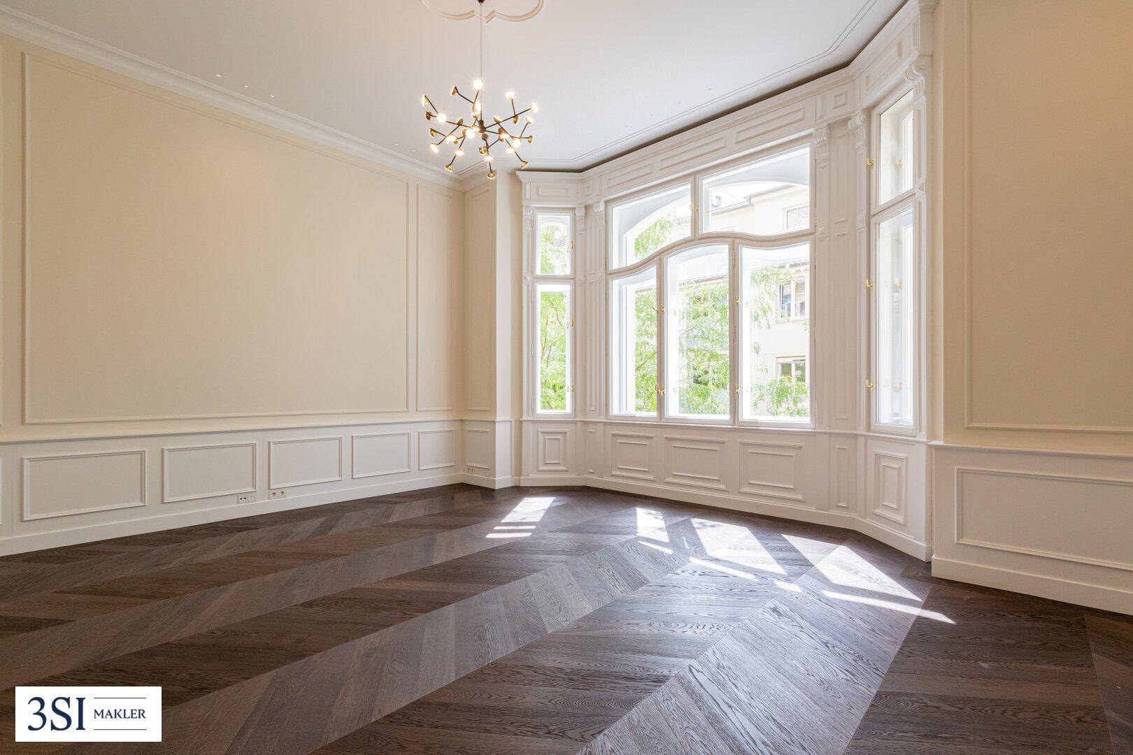 Lichtdurchfluteter Wohnraum mit Erkerfenstern, dunklem Parkett und moderner Beleuchtung.