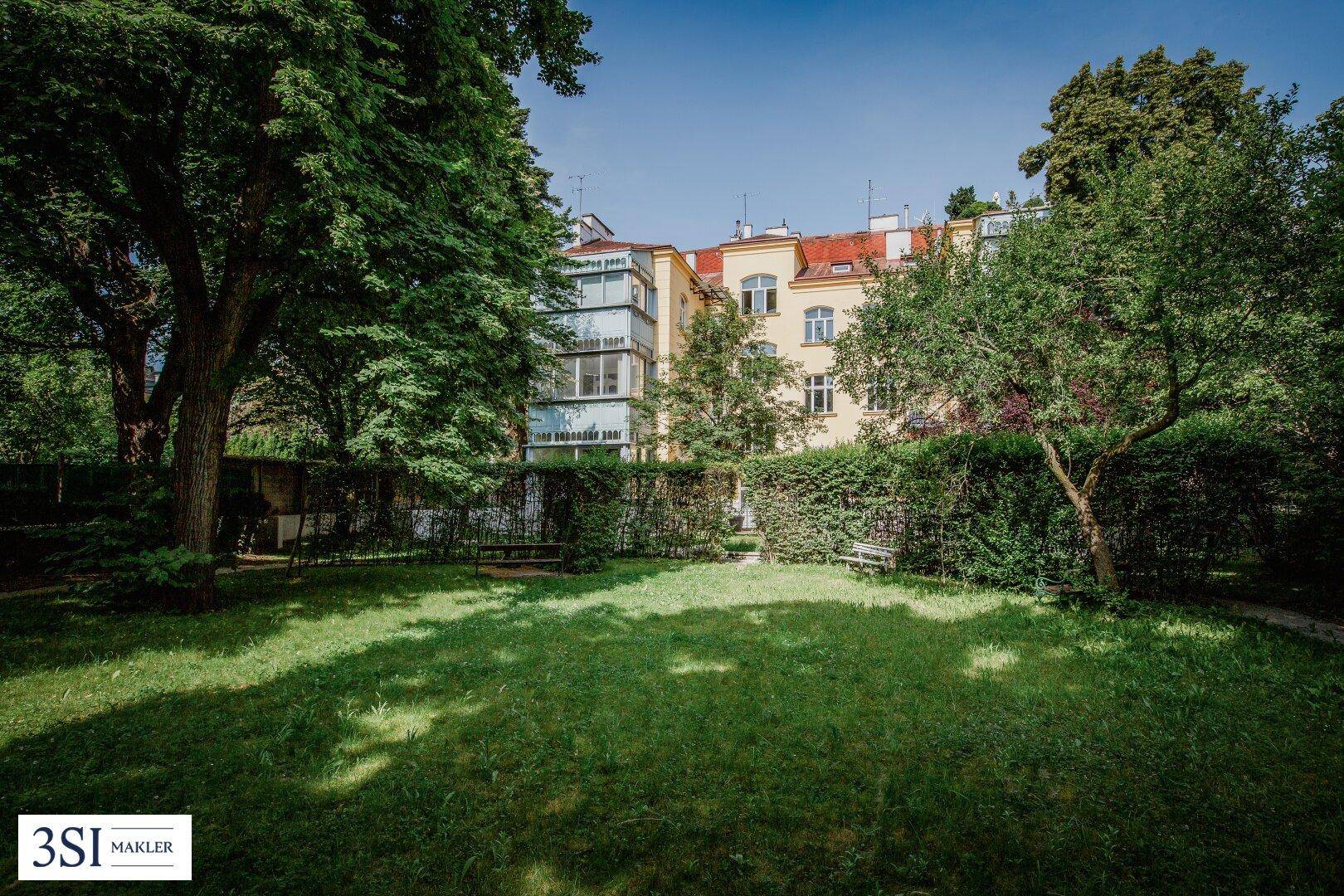 Weitläufiger Gartenbereich mit Rasenfläche, hohen Hecken und altem Baumbestand.