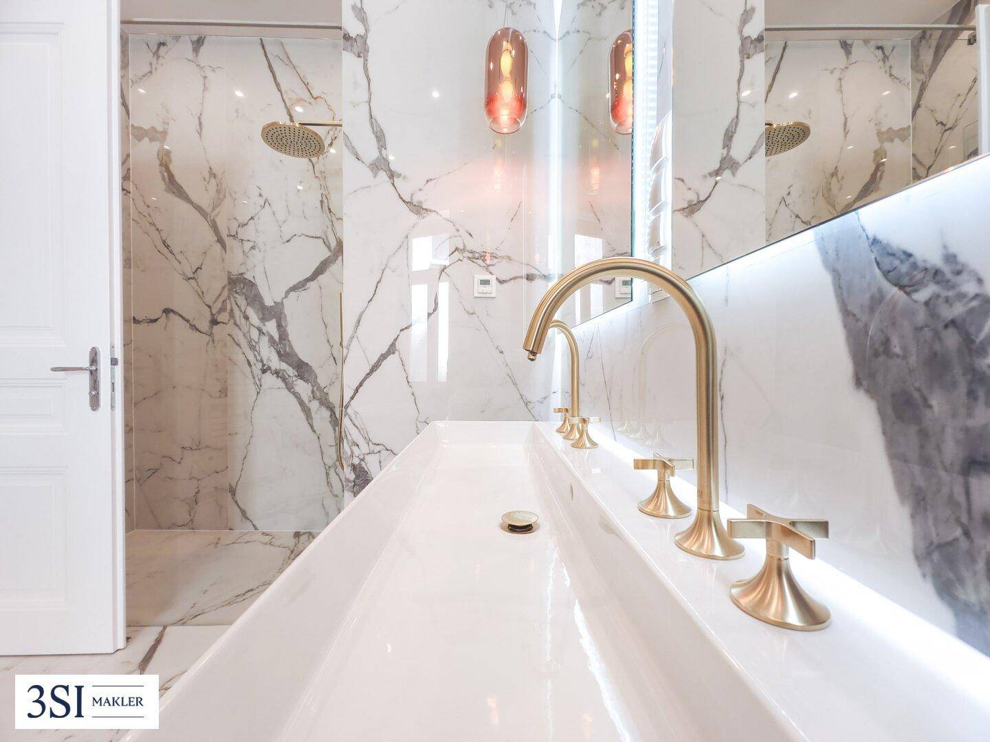 Detailansicht des modernen Waschbeckens mit goldenen Armaturen und Marmorfliesen im Badezimmer.
