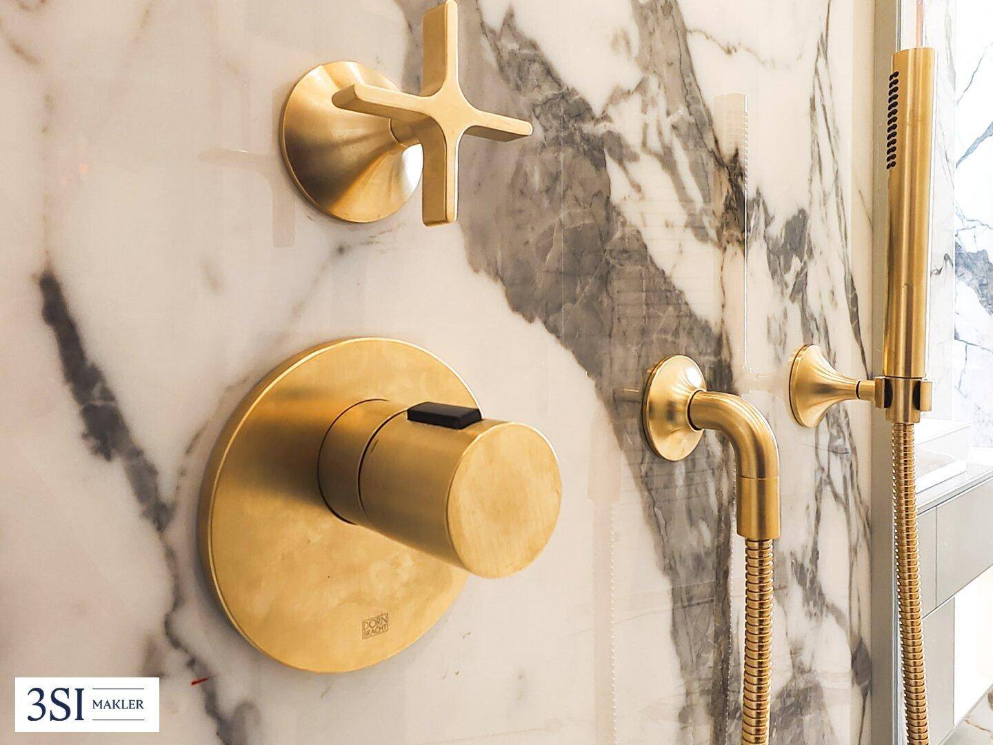 Nahaufnahme der eleganten goldenen Duscharmaturen an einer Marmorwand im Badezimmer.