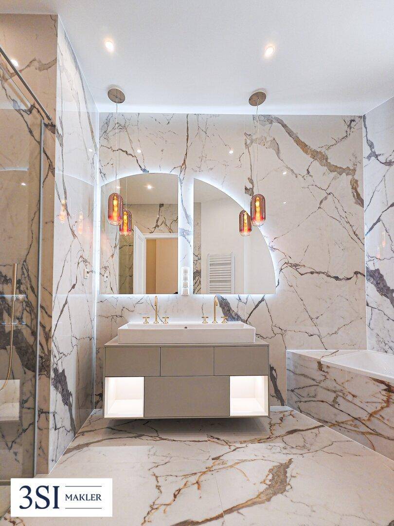 Luxuriöses Badezimmer mit Marmorfliesen, Doppelwaschbecken und modernen Leuchten.