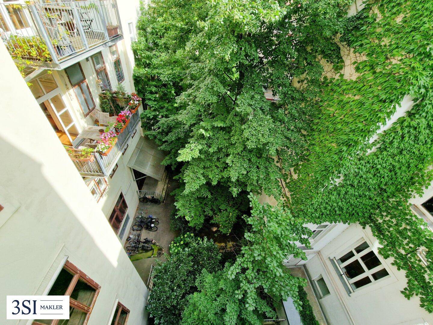 Vogelperspektive auf den grünen Innenhof mit Bäumen, begrünten Wänden und mehreren Balkonen.