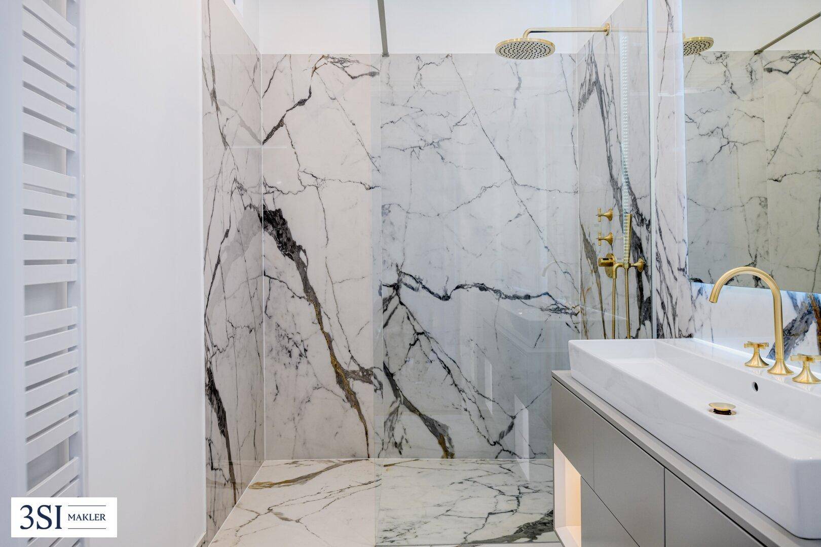 Elegantes Badezimmer mit Marmorwänden, begehbarer Dusche und goldfarbenen Armaturen.