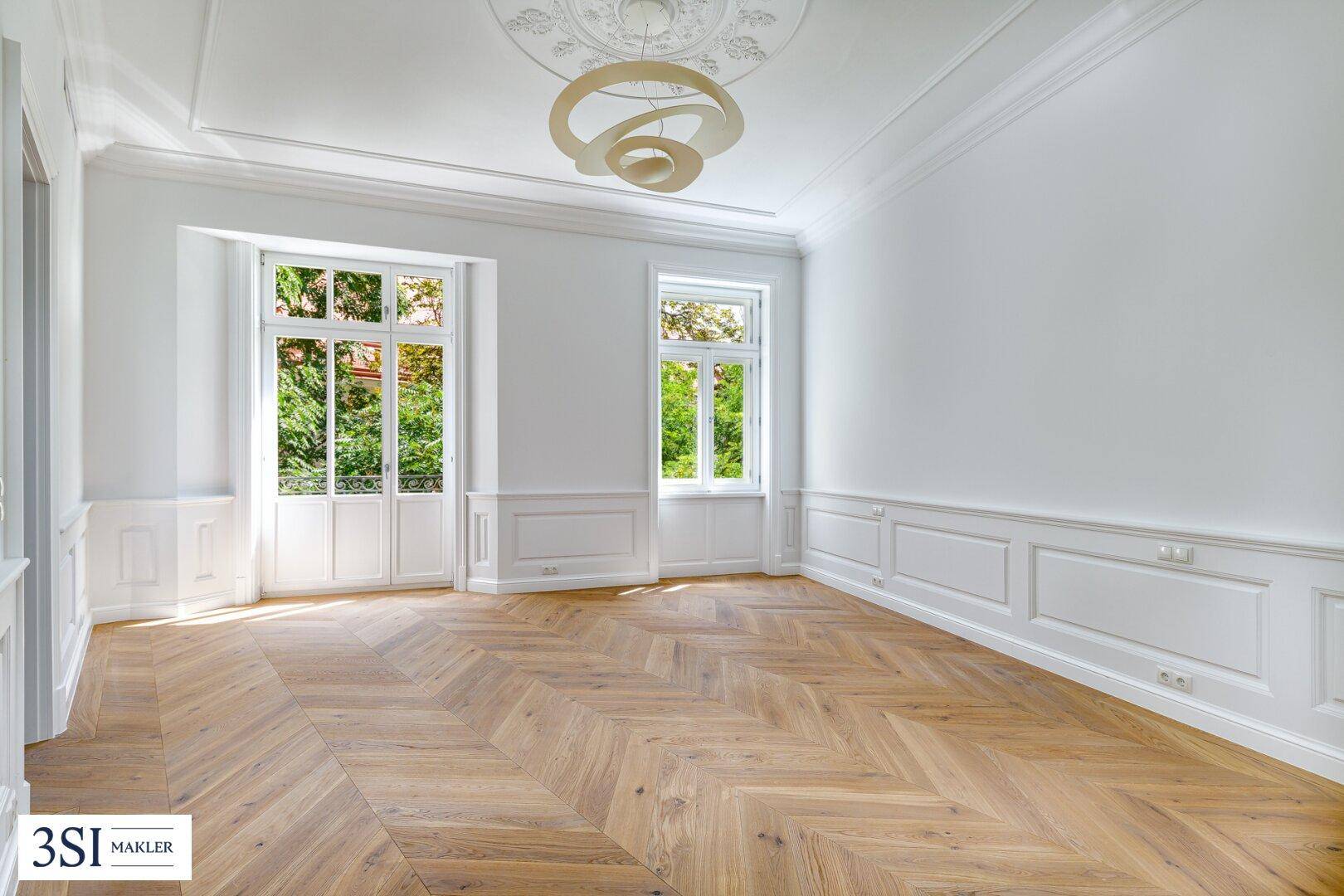 Geräumiges Zimmer mit Fischgrätparkett, hohen Decken und Stuckverzierungen.