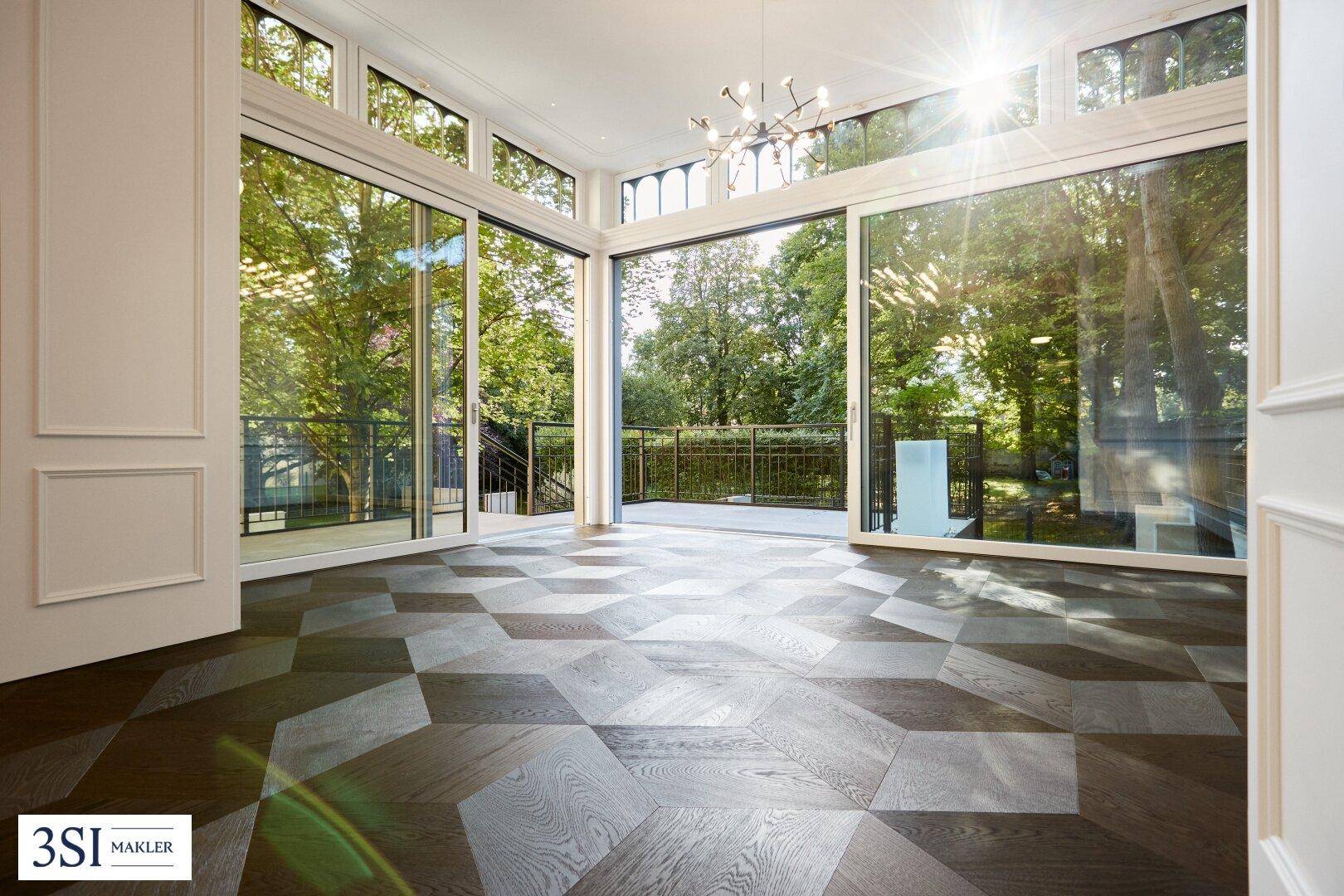 Heller Wohnraum mit großen Fenstern, geometrischem Parkettboden und Zugang zu einem Balkon.