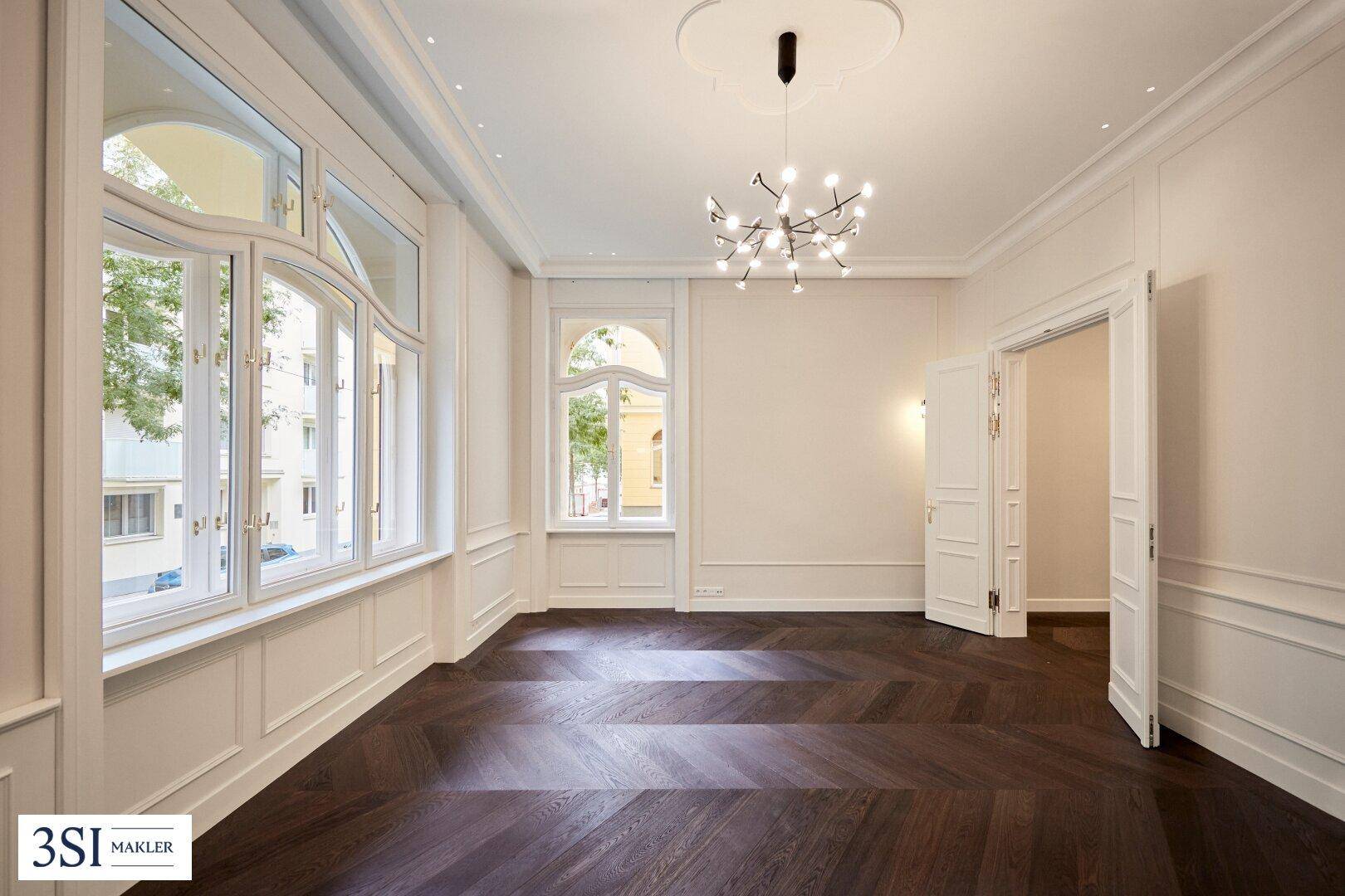 Elegantes Wohnzimmer mit großen Bogenfenstern, dunklem Parkettboden und hohen Decken.