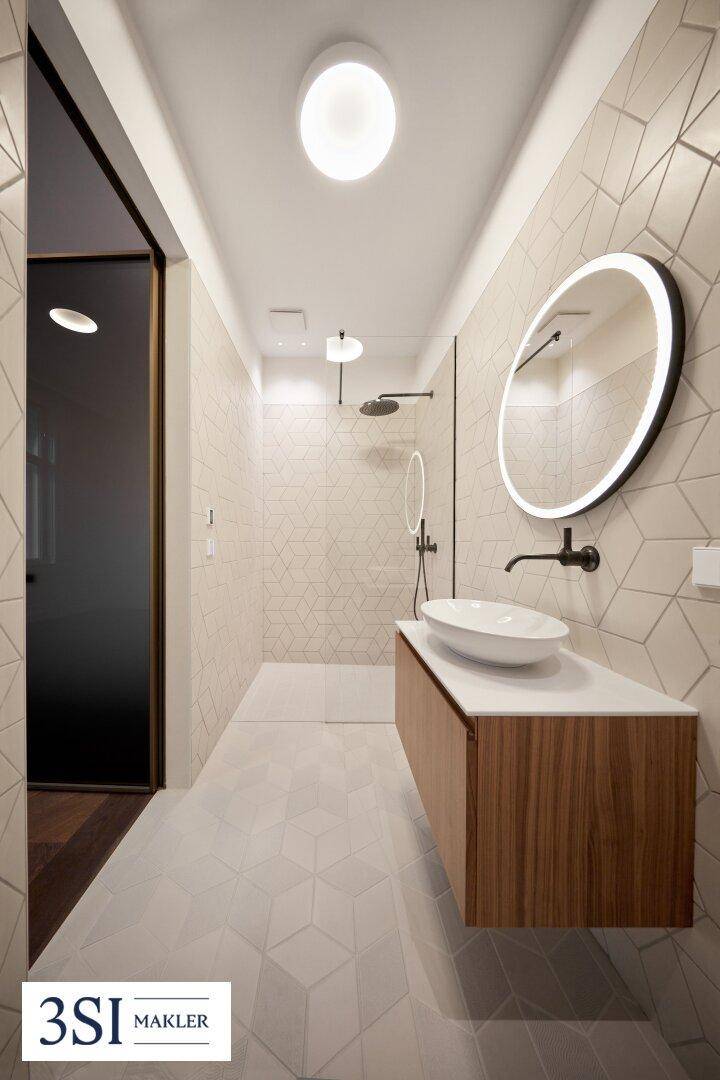Modernes Badezimmer mit begehbarer Dusche, schwebendem Waschtisch und beleuchtetem Spiegel.