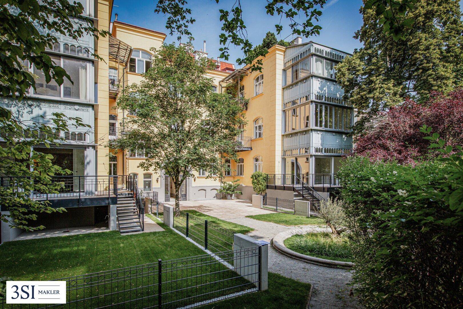 Attraktives Gebäude mit gelber Fassade und modernem Glasanbau, umgeben von üppigem Grün.