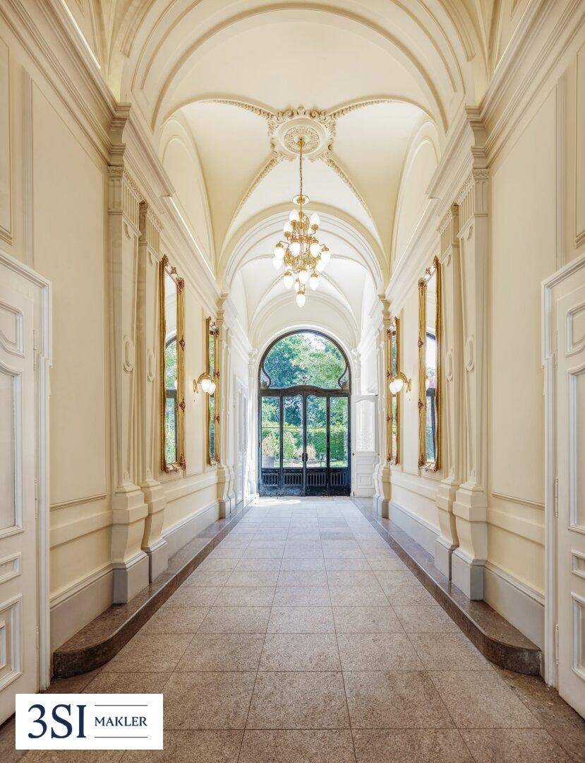 Eleganter Flur mit hohen Gewölbedecken, Stuckverzierungen und großen Fenstern zum Garten.