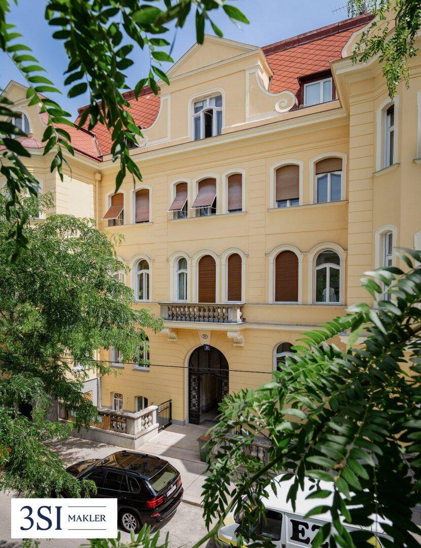 Historische Fassade des Gebäudes mit gelbem Anstrich, Balkon und gepflegter Umgebung.