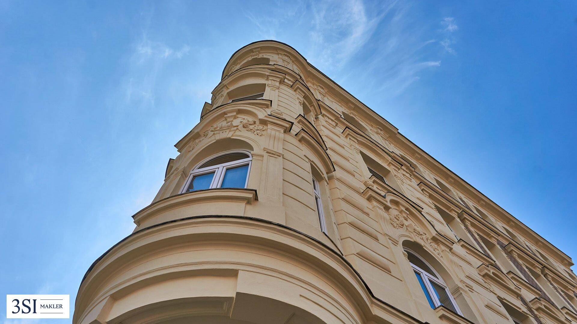 Architektonische Detailansicht der abgerundeten Gebäudeecke mit Stuckverzierungen unter blauem Himmel.