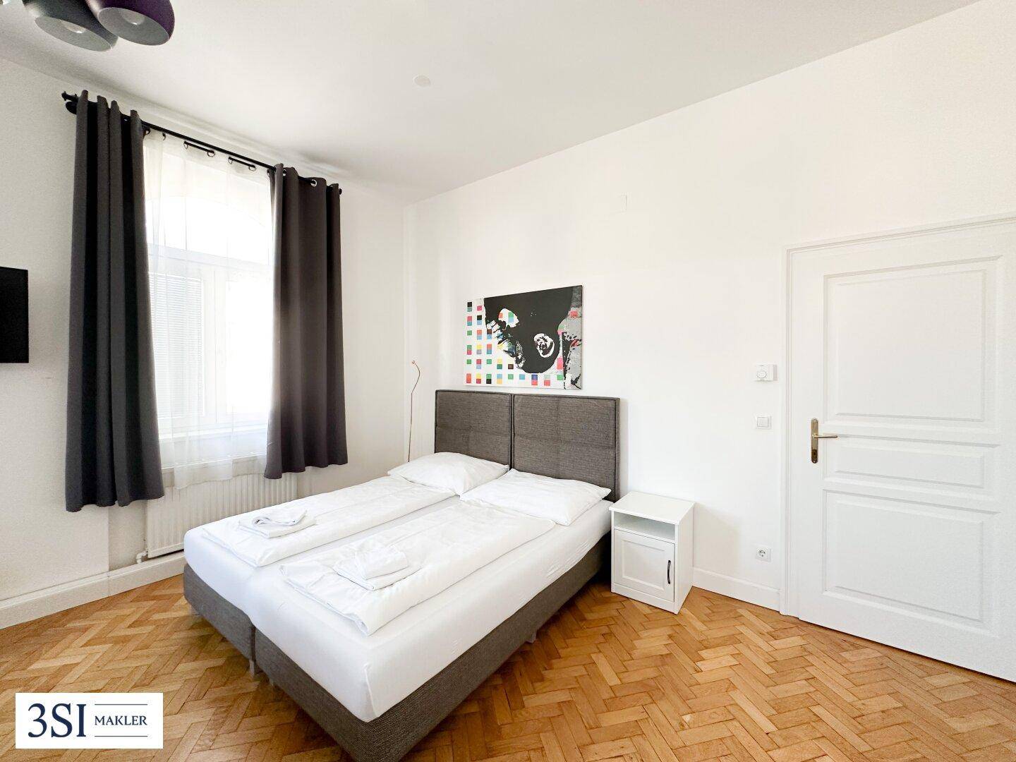 Gemütliches Schlafzimmer mit Doppelbett, Fischgrätparkett und viel Tageslicht.