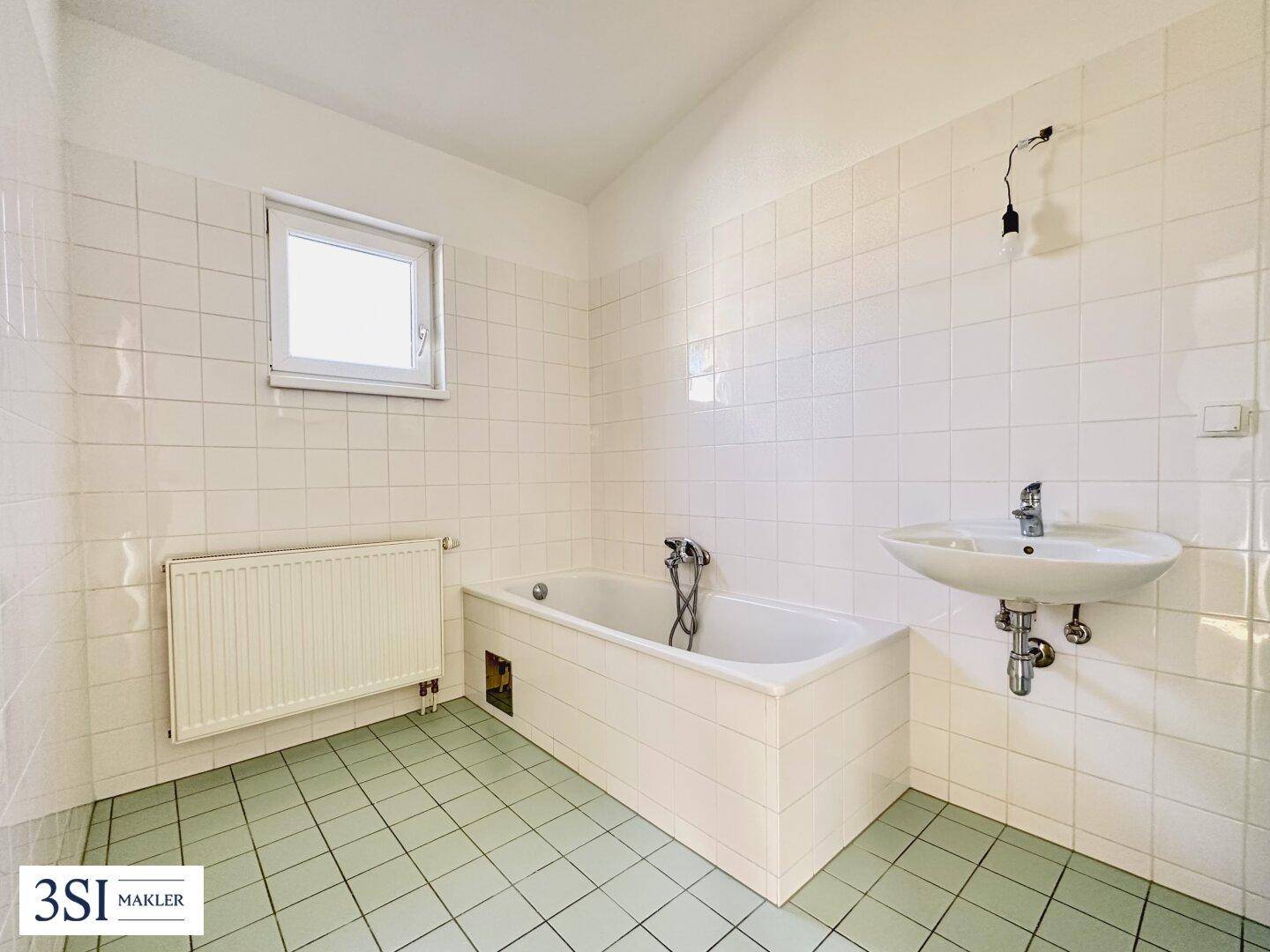 Badezimmer mit Badewanne, Waschbecken und hellgrünen Fliesen, ausgestattet mit einem Fenster.