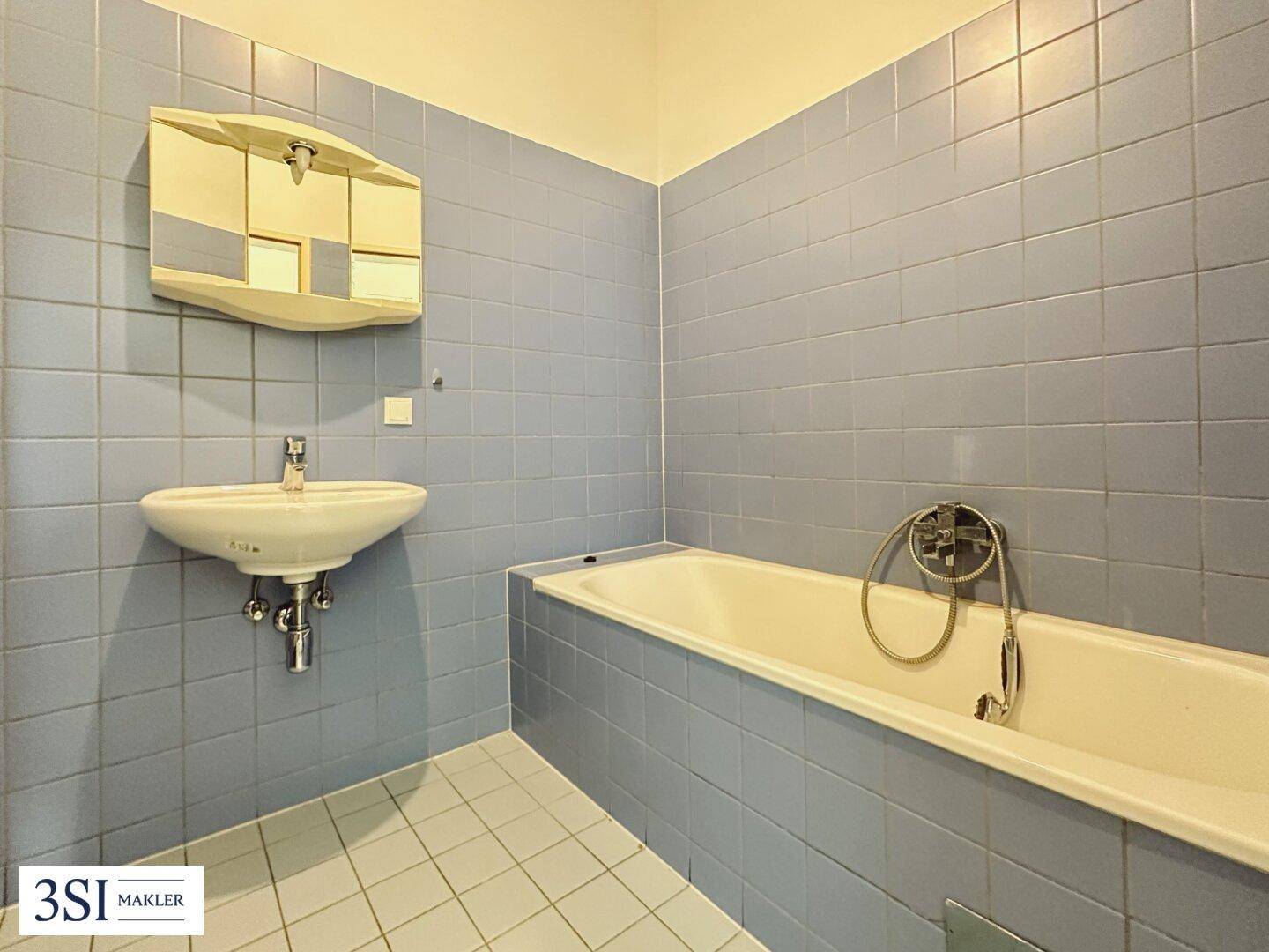 Badezimmer mit blauen Fliesen, Badewanne und Waschbecken, im Stil der 80er Jahre.