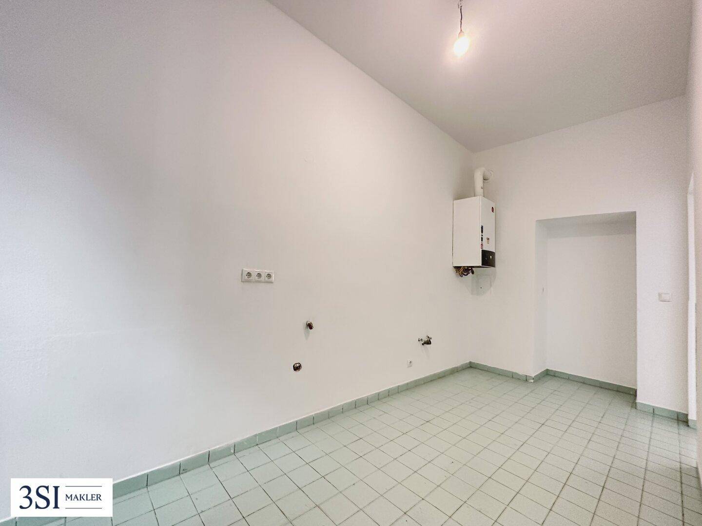 Leerer Raum mit hellgrünen Bodenfliesen und Wandanschluss für einen Warmwasserbereiter.