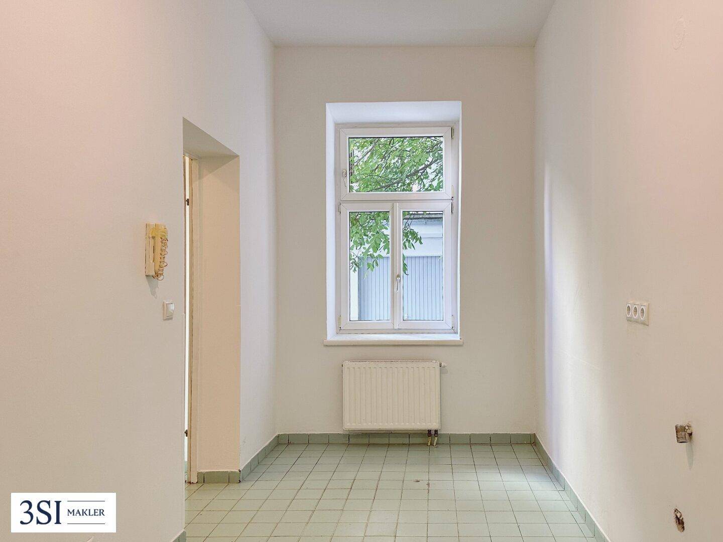 Heller Raum mit Fenster, Heizkörper und hellgrünen Bodenfliesen, der viel natürliches Licht bietet.