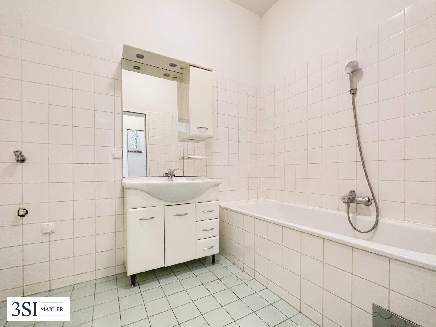 Helles Badezimmer mit weißen Wand- und Bodenfliesen, Badewanne und Waschbecken mit Spiegelschrank.