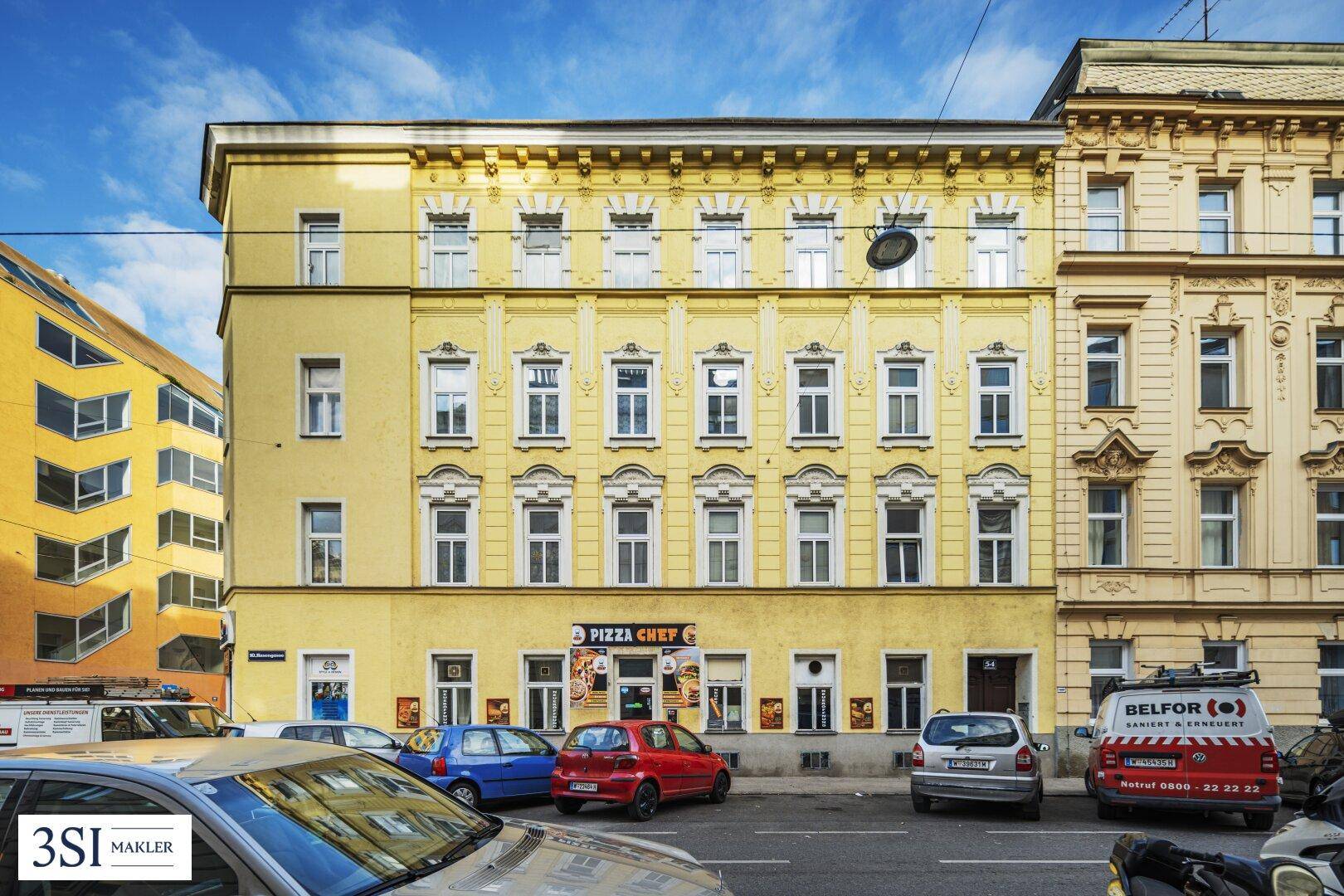 Fassade eines Wohnhauses mit gelbem Anstrich, vielen Fenstern und Geschäften im Erdgeschoss.