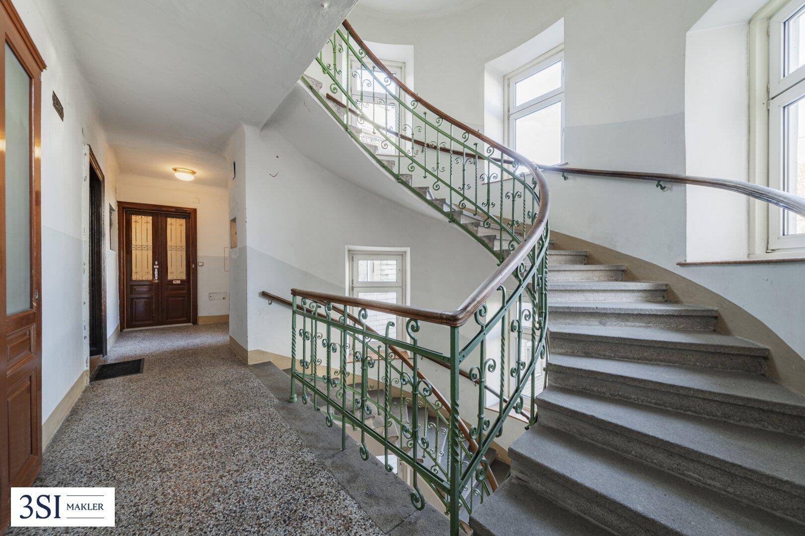 Historisches Treppenhaus mit geschwungenem Geländer und Terrazzoboden in einem Altbau.