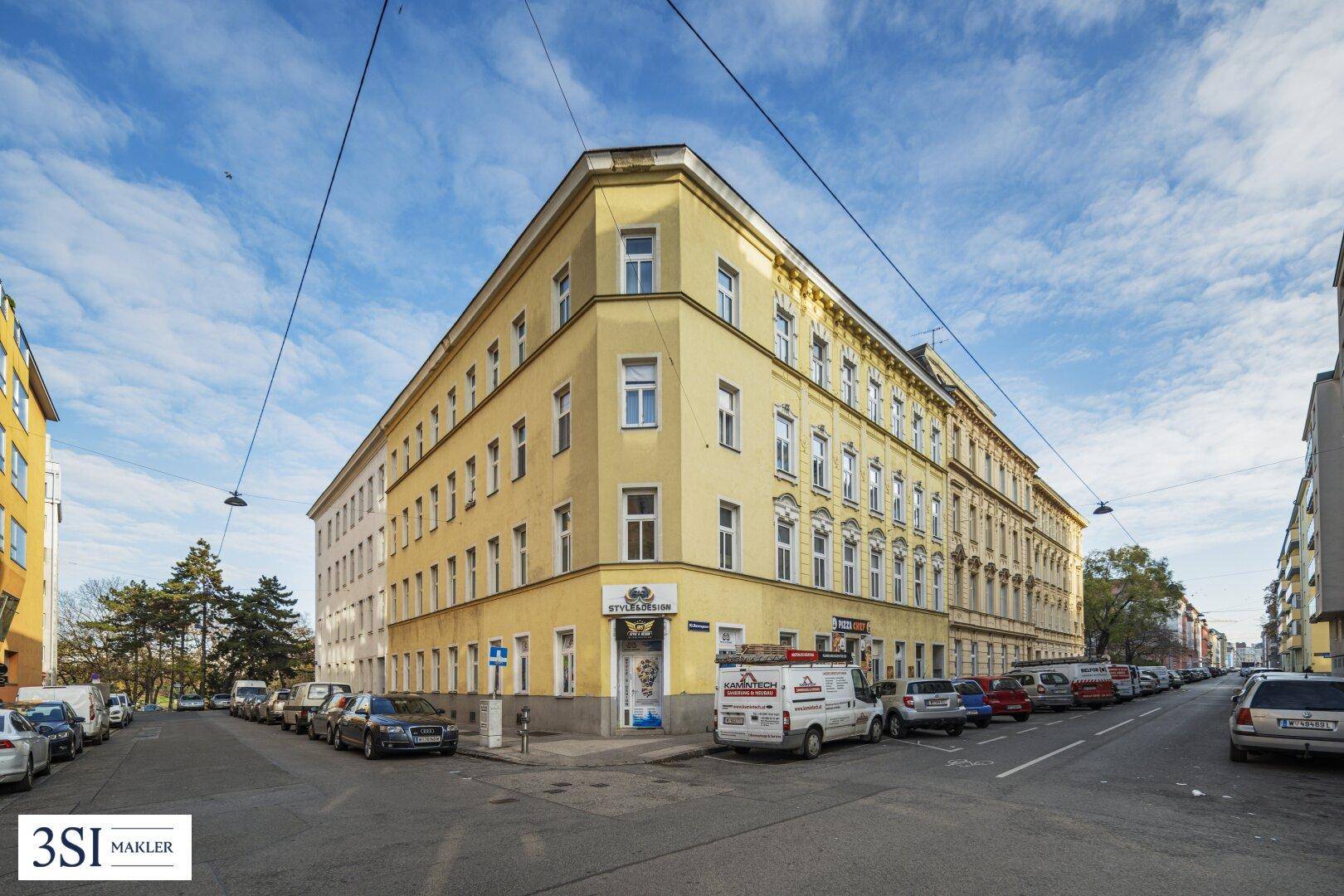 Straßenansicht eines Eckgebäudes mit gelber Fassade und Geschäften im Erdgeschoss.