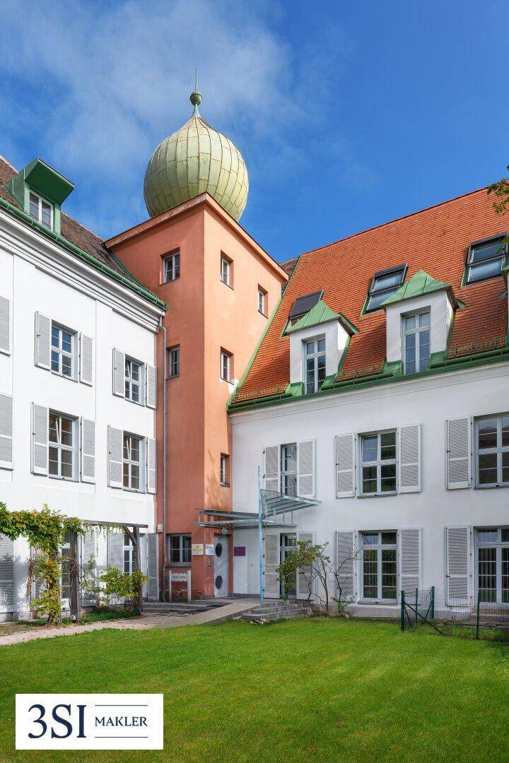 Historisches Anwesen mit weißer Fassade, rotem Dach und markantem Turm, umgeben von einer gepflegten Rasenfläche.