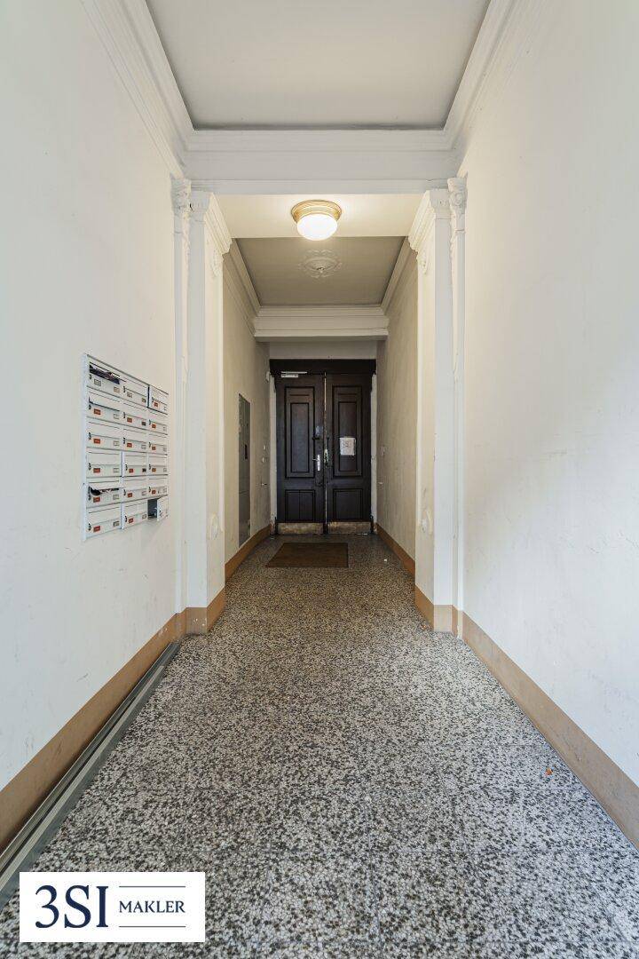 Eingangsbereich eines Altbaus mit Terrazzoboden und hohen Decken, führt zu den Wohnungen.