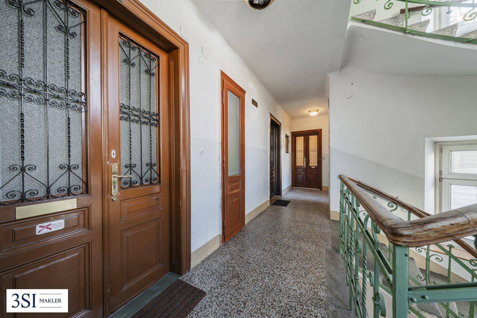 Heller Hausflur mit Terrazzoboden, Holztüren und historischem Treppengeländer in einem Altbau.