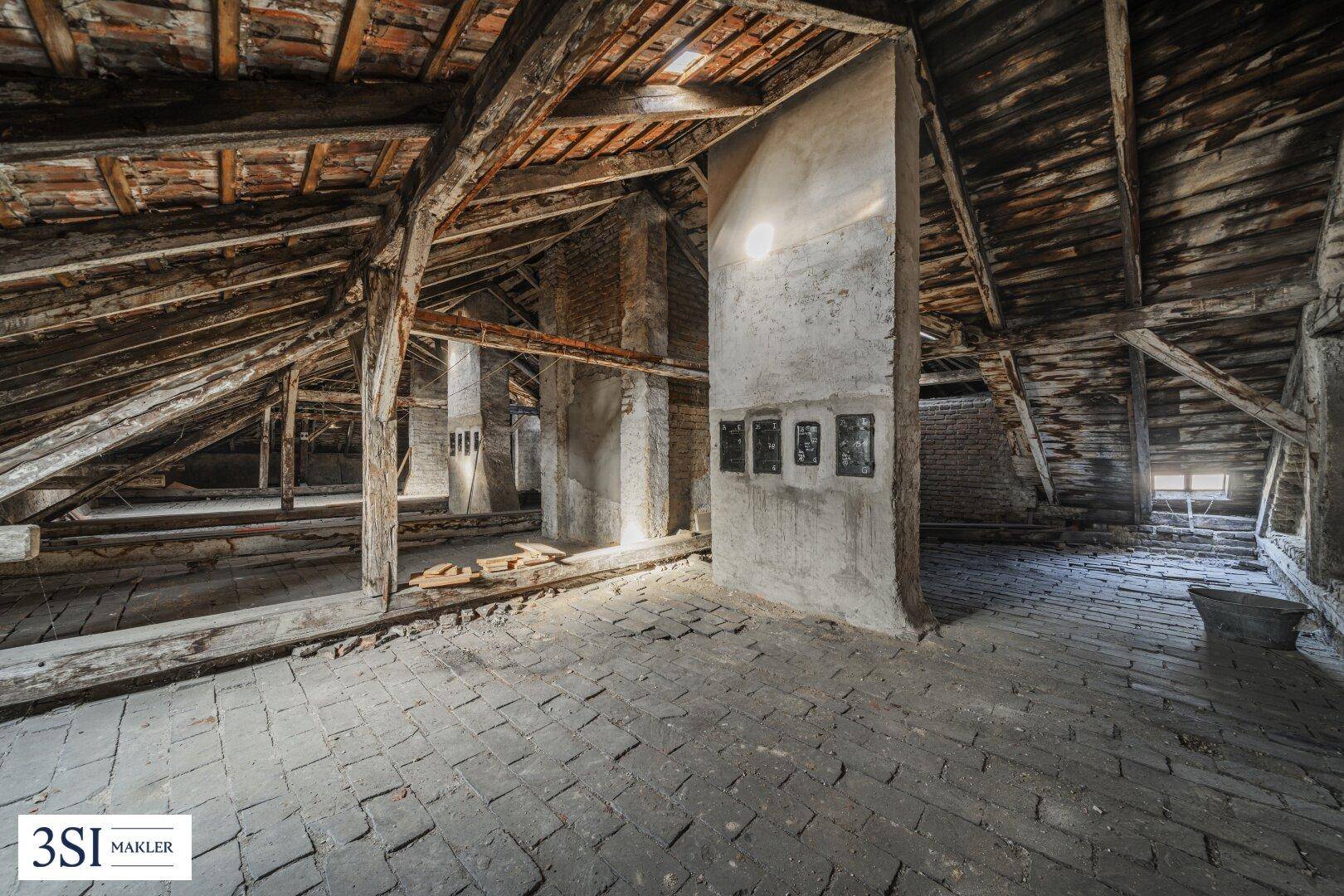 Geräumiger Dachboden mit sichtbaren Holzbalken und Ziegelboden, bereit für den Ausbau.