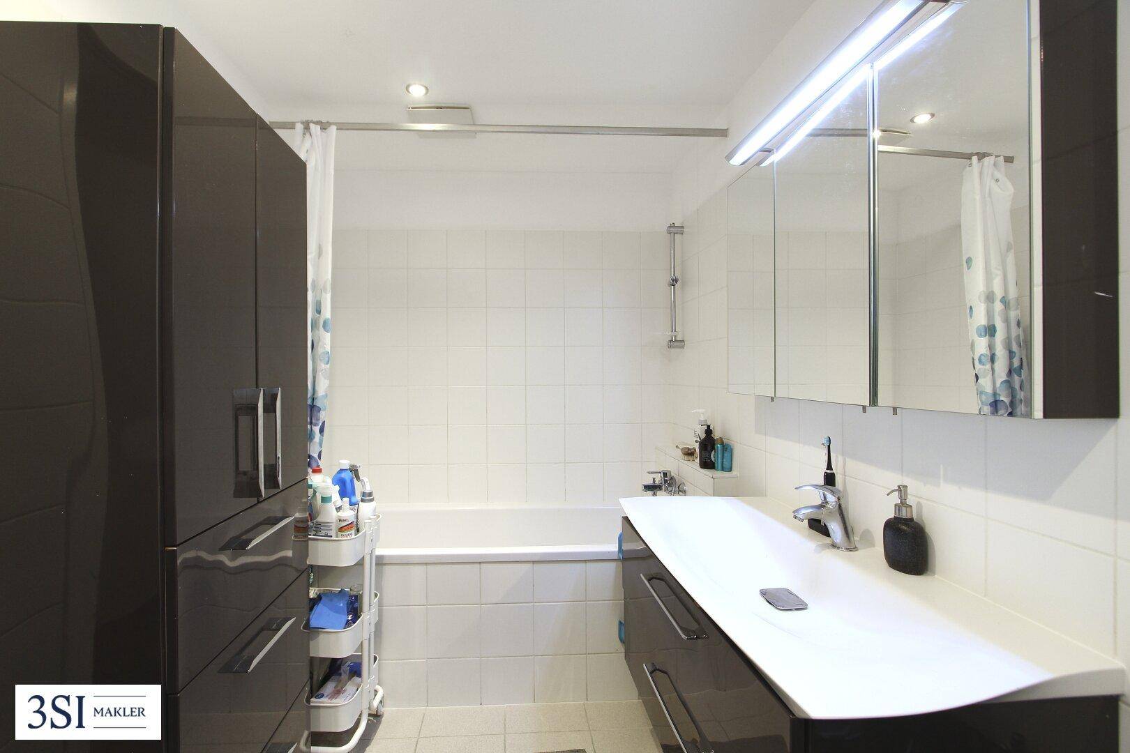 Modernes Badezimmer mit Badewanne, Waschtisch und Spiegelschrank, ergänzt durch einen hohen Schrank.
