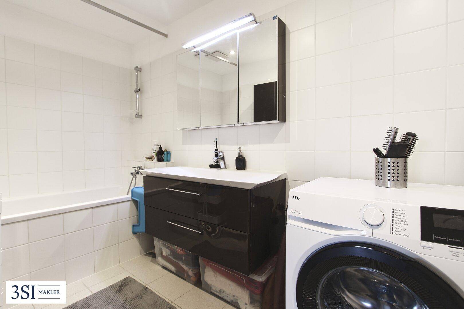 Funktionales Badezimmer mit Badewanne, Waschtisch, Spiegelschrank und integrierter Waschmaschine.