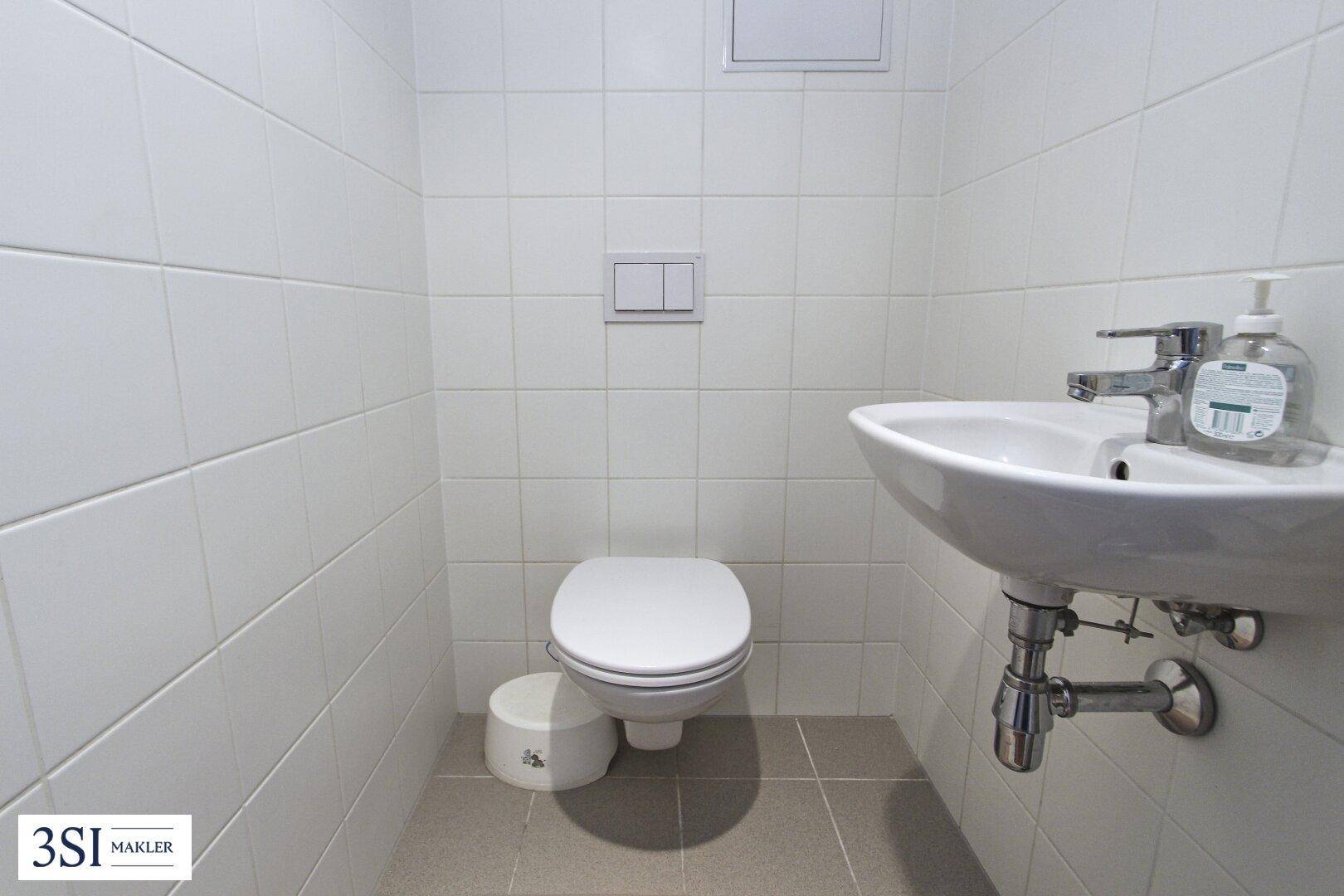 Kleines Gäste-WC mit Toilette und Handwaschbecken, komplett gefliest in hellem Weiß.