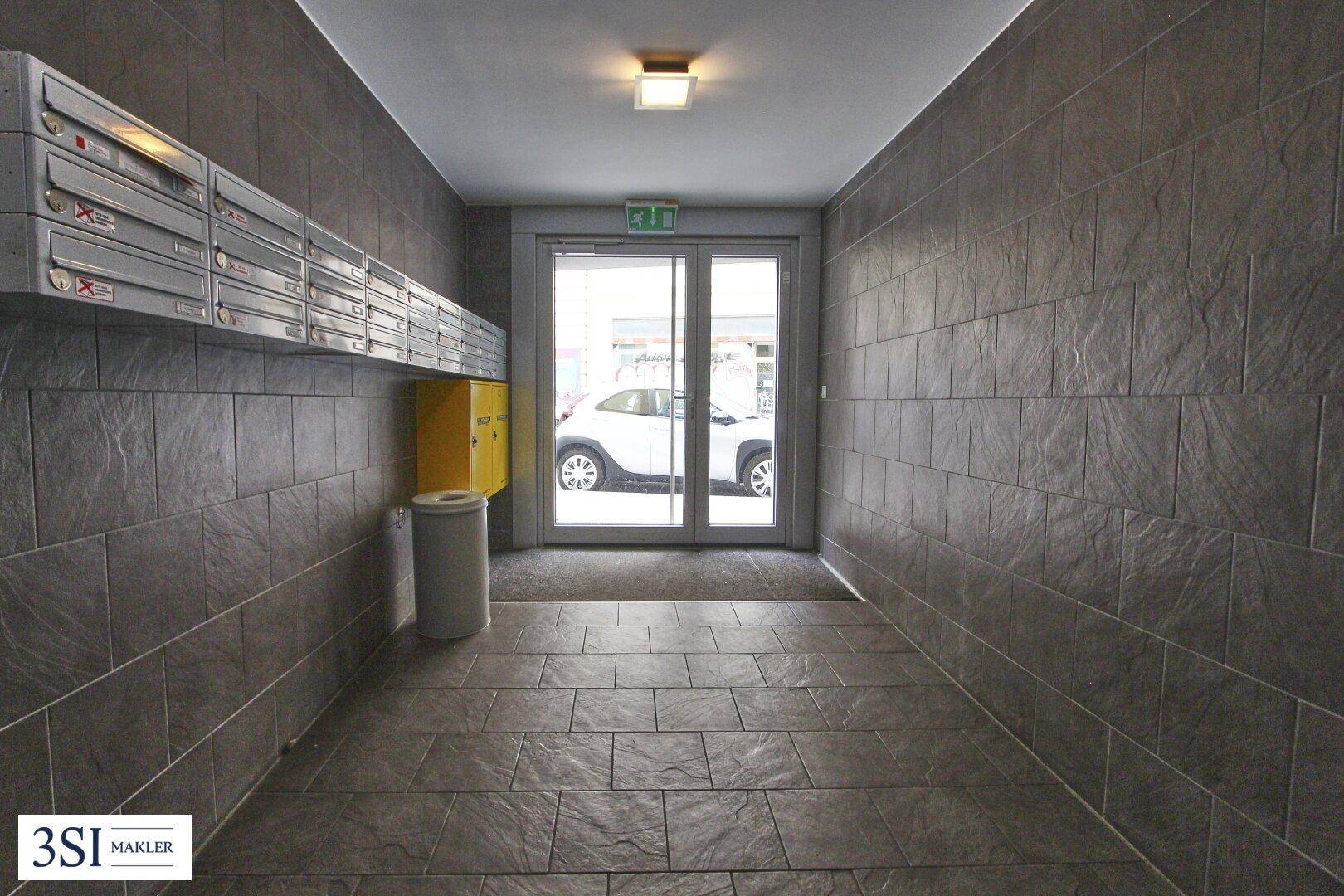 Eingangsbereich des Gebäudes mit Briefkästen, gefliesten Wänden und einer Glastür zur Straße.