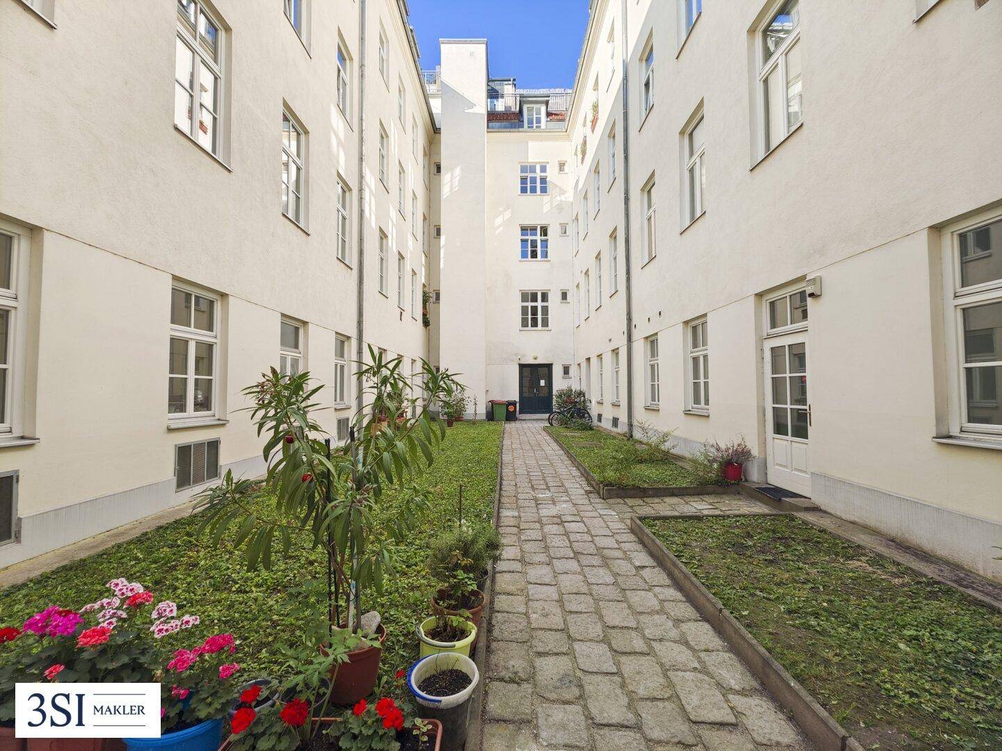 Grüner Innenhof mit gepflastertem Weg und bepflanzten Beeten, umgeben von Wohngebäuden.