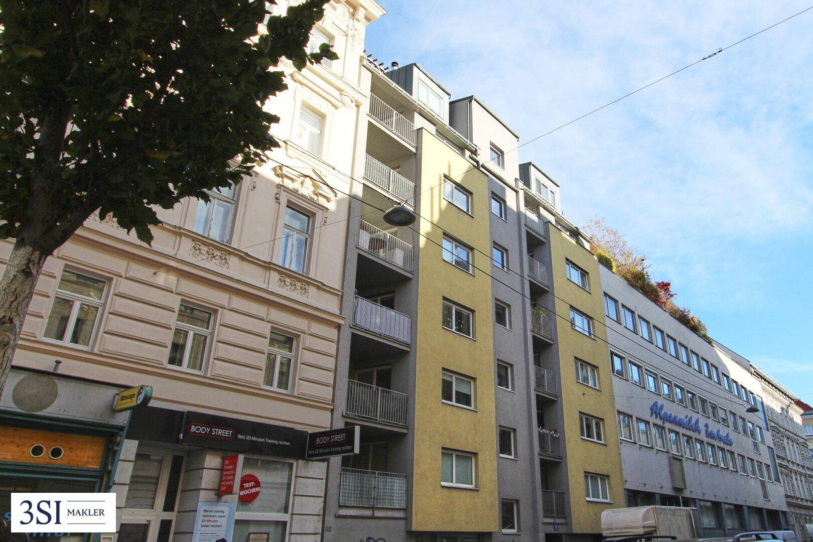 Ansicht der modernen Gebäudefassade mit gelben und grauen Elementen sowie Balkonen in einer städtischen Straße.